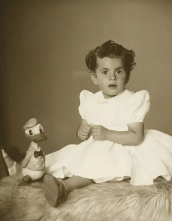 [Niñita de vestido blanco con el Pato Donald de juguete, sentada sobre una piel blanca]  [fotografía] Kyutaro Tunekawa.