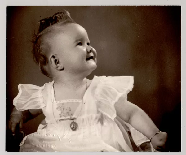 [Bebé de pelo rizado, con un vestido de gasa; lleva una medalla, aros y pulsera]  [fotografía] Kyutaro Tunekawa.