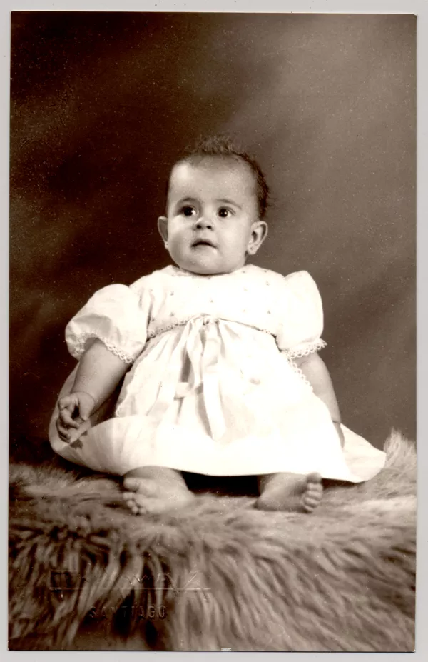 [Niñita de vestido recogido con una cinta blanca, mangas cortas globo y descalza; sentada sobre un felpudo]  [fotografía] Kyutaro Tunekawa.