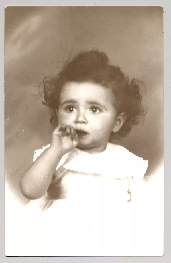 [Niñita de vestido blanco con vuelos pelo crespo ojos grandes y un dedo metido en la boca]  [fotografía] Kyutaro Tunekawa.