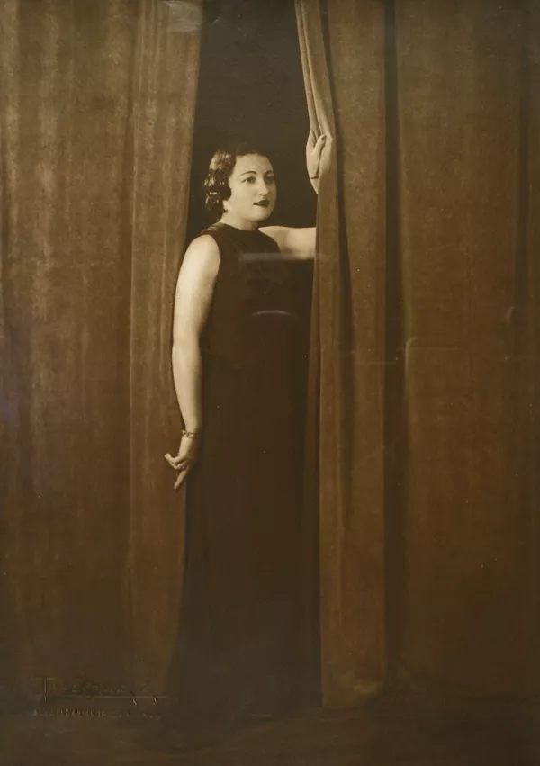 [Mujer joven, vestida de largo, posa de pie entre dos cortinas]  [fotografía] Kyutaro Tunekawa.