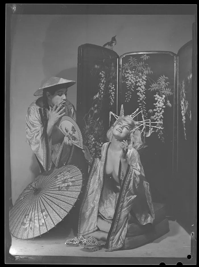 [Jenny Morán, con abanico, caracerizada como japonesa, junto a otro; ambientacón fotográfica: biombo y quitasol japoneses]  [fotografía] Alfredo Molina Lahitte.