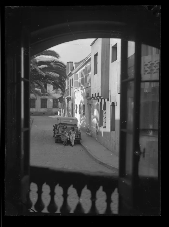 [Barrio residencial de estilo ecléctico: Joven mujer junto a dos niños, sentados en la parte posterior de un auto]  [fotografía] Alfredo Molina Lahitte.