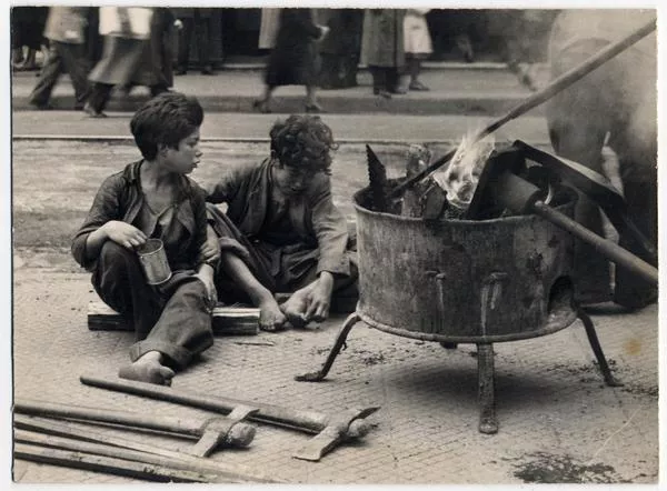 Pavimentación de calle Ahumada y levantamiento de rieles de tranvías : [Pobreza infantil; niños sentados junto a un fogón]. [fotografía] Domingo Ulloa.
