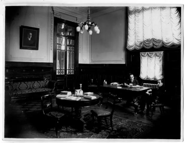 [Biblioteca Nacional 1927. Salones interiores, con mesa redonda y retangular, con dos personas sentadas]  [fotografía].