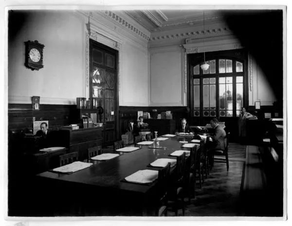 [Biblioteca Nacional 1927. Salones interiores, con una mesa rectangular y varias personas]  [fotografía].