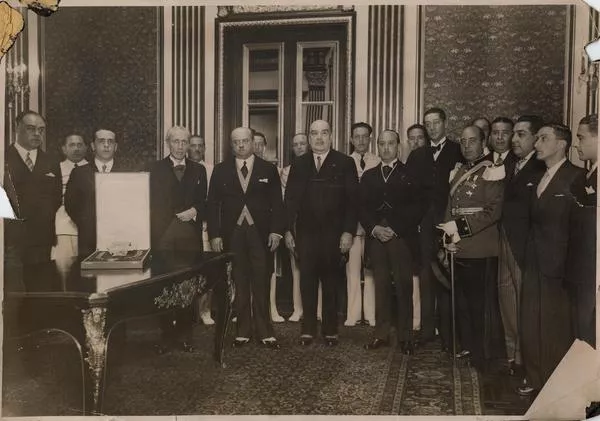 [Retrato de Manuel Rivas Vicuña, junto a un grupo de personas, en una ceremonia de condecoración; En una mesita, se encuentra la caja que guarda la distinción]  [fotografía]