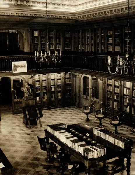[Vista interior de la Biblioteca Americana Barros Arana, Sala Medina, Biblioteca Nacional: espacio revestido en madera de nogal, Anaqueles con puerta de vidrio, parquet de maderas nobles, lámparas de techo en bronce, de 8 brazos con bombillas como velas, balconada en el segundo piso, busto de Barros Arana]  [fotografía].