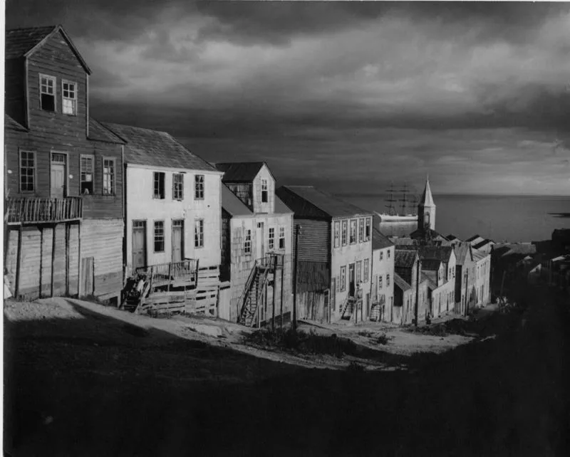 [Viviendas en una calle de Achao, se aprecia la torre de una iglesia y la bahía]  [fotografía] Jorge Opazo Galindo.