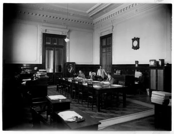 [Biblioteca Nacional 1927. Salones interiores, con una mesa rectangular y cuatro personas]  [fotografía].