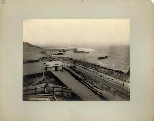 [Vista panorámica del puerto, se divisan vías férreas a orillas del mar, unas casas de la faena, y barcos en el mar]  [fotografía].