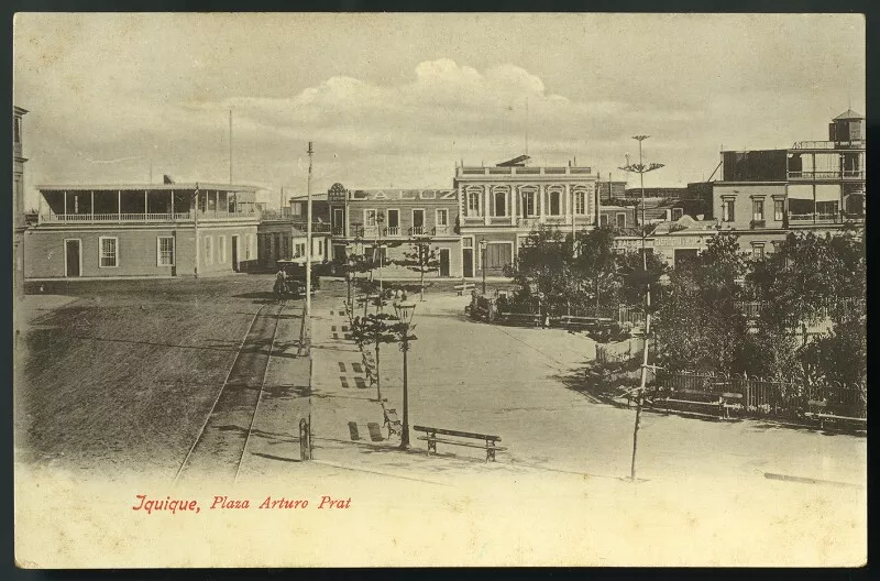 Iquique - Plaza Arturo Prat : [Vista parcial de la plaza, edificios que la rodean, almacenes "La Luz", "Taller de Gasfitería y hojalata", entre otros] [fotografía] Carlos Brandt.