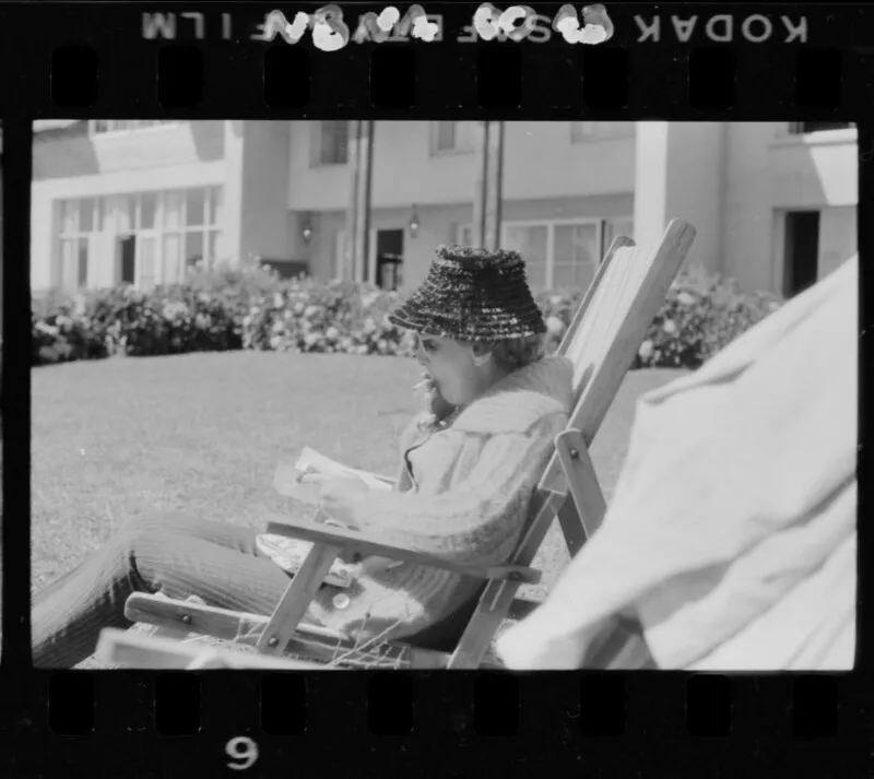 [Mujer fumando mientras lee en el jardín de su casa]  [fotografía] Antonio Quintana.