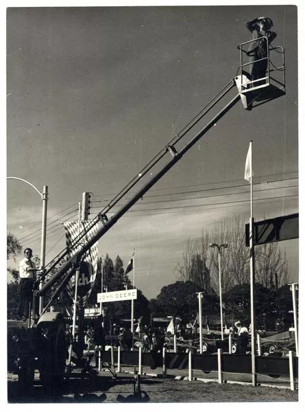 [Domingo Ulloa; suspendido en el aire sobre una escalera mecánica, toma fotos de la Exposición Ganadera de la Quinta Normal].  [fotografía]