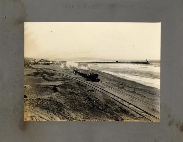 [Vista de una locomotora de carga, pasando por la orilla del mar]  [fotografía].